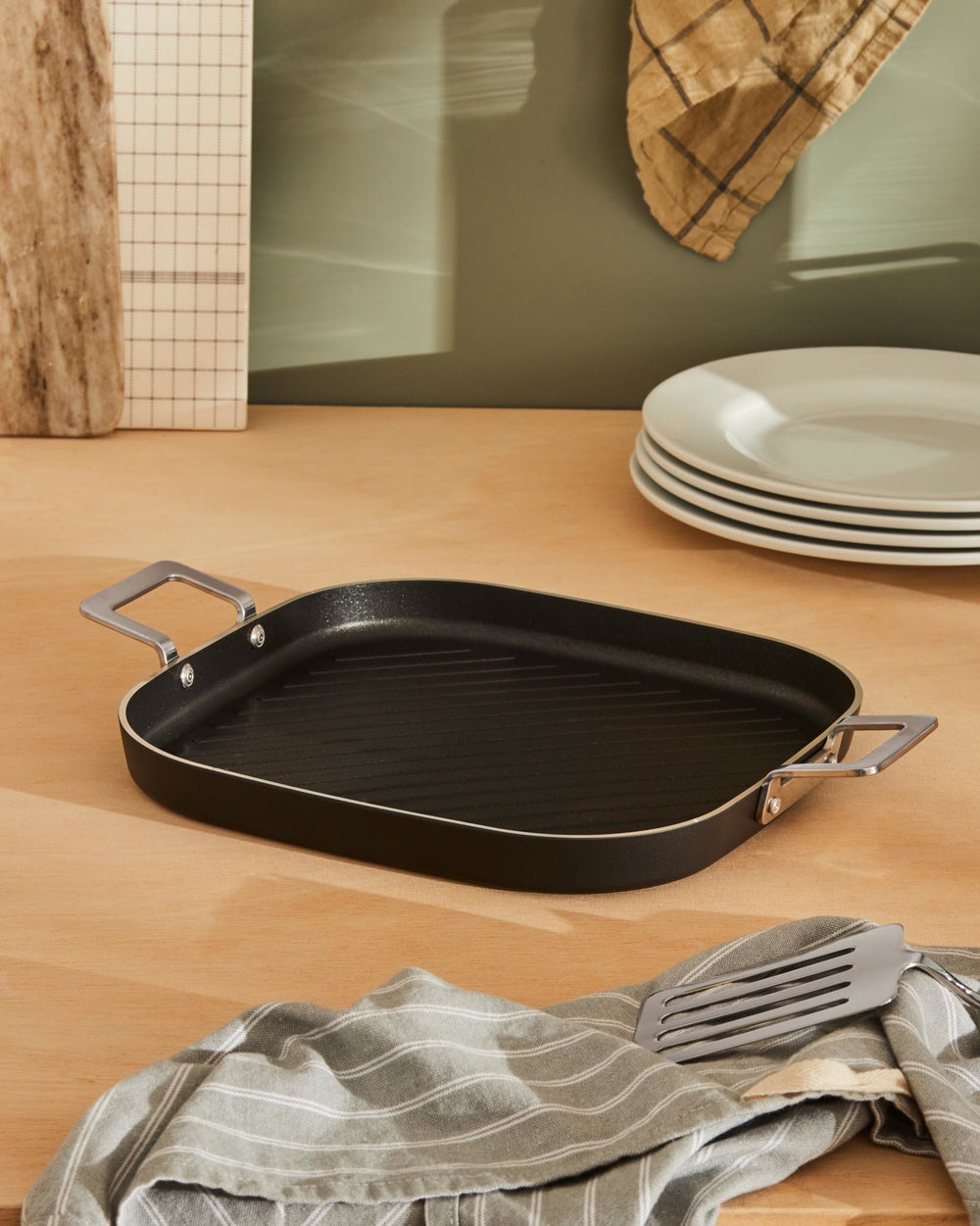 Black rectangular grill pan by Alessi with ribbed surface and silver handles on a wooden table.