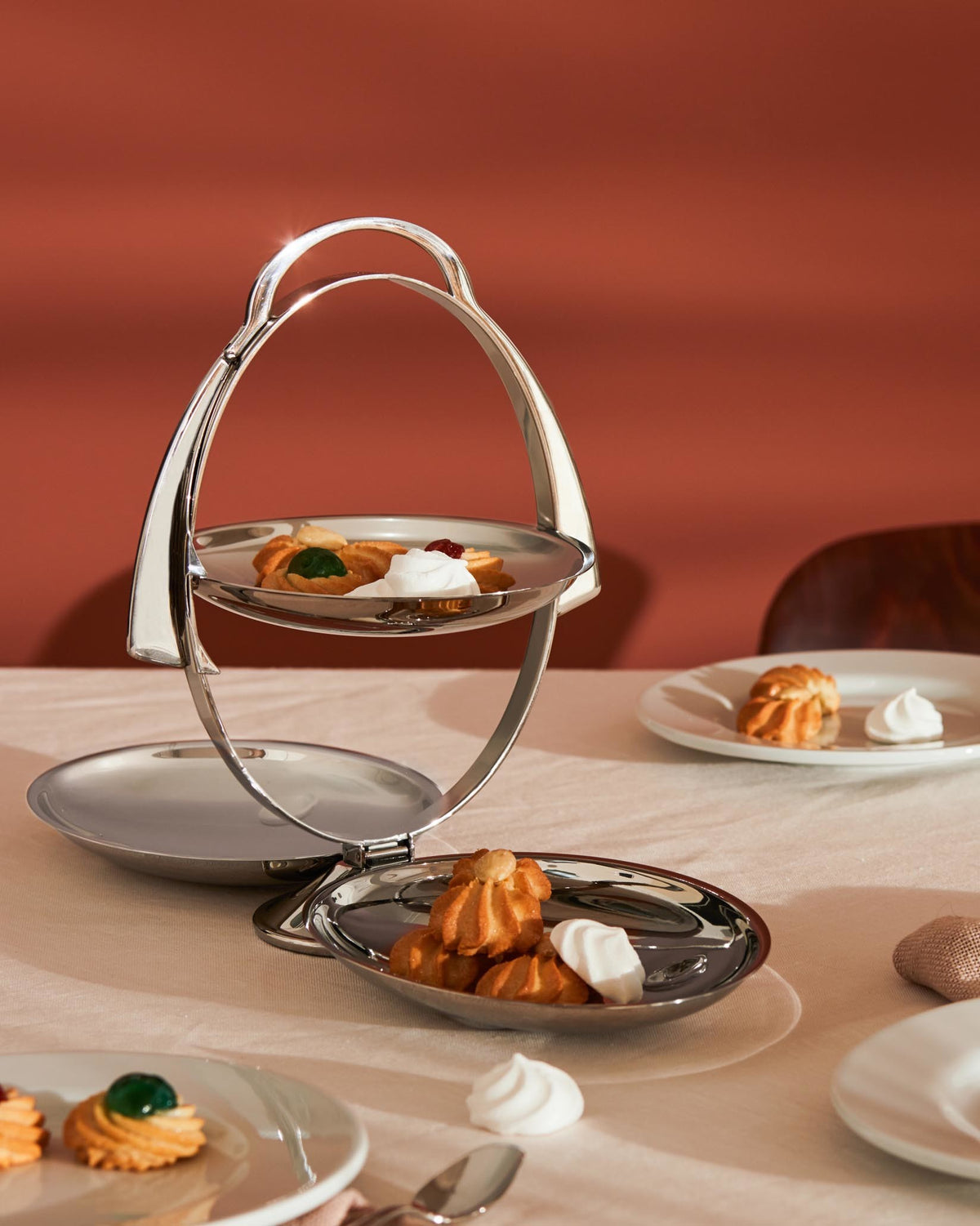 Foldable silver metal tiered serving stand by Alessi, displaying assorted cookies and meringues.
