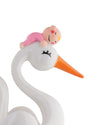 White, glossy baby-themed decorative figure by Alessi, depicting a stork with an orange beak carrying a baby in pink.