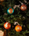 Colorful Madonna Christmas ornaments by Alessi, with unique character faces, hanging on a festive green tree.