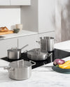 Brushed stainless steel Convivio pots and pans by Alessi, displayed on a modern induction hob in a minimalist kitchen.