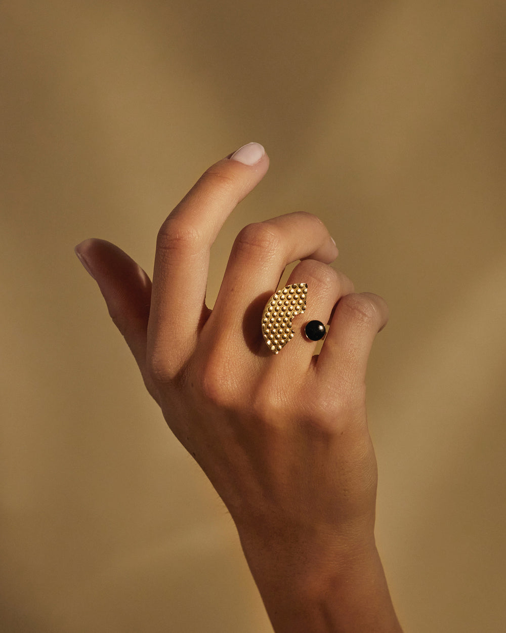 Gold-toned Edone ring by Alessi, with a fan-shaped studded design and a black spherical accent, worn on a hand.