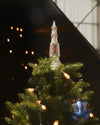 White Holyhedrics tree topper and blue ornament by Alessi, featuring colorful pixelated patterns on a green tree.