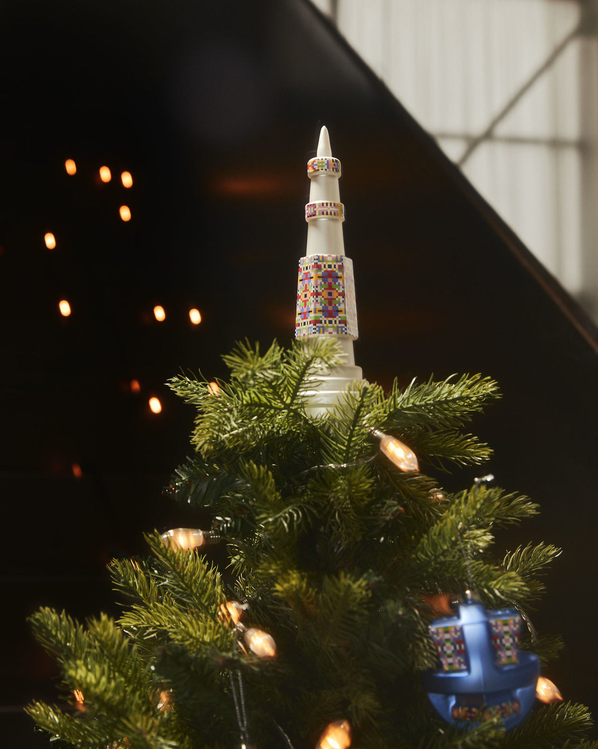 White Holyhedrics tree topper and blue ornament by Alessi, featuring colorful pixelated patterns on a green tree.
