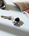 Open silver spherical keychain container by Alessi, revealing a black interior, with a 'BON BON' coin nearby.