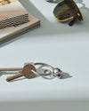 Silver-toned mouse-shaped keychain by Alessi, its reflective metal surface lying on a light blue table.