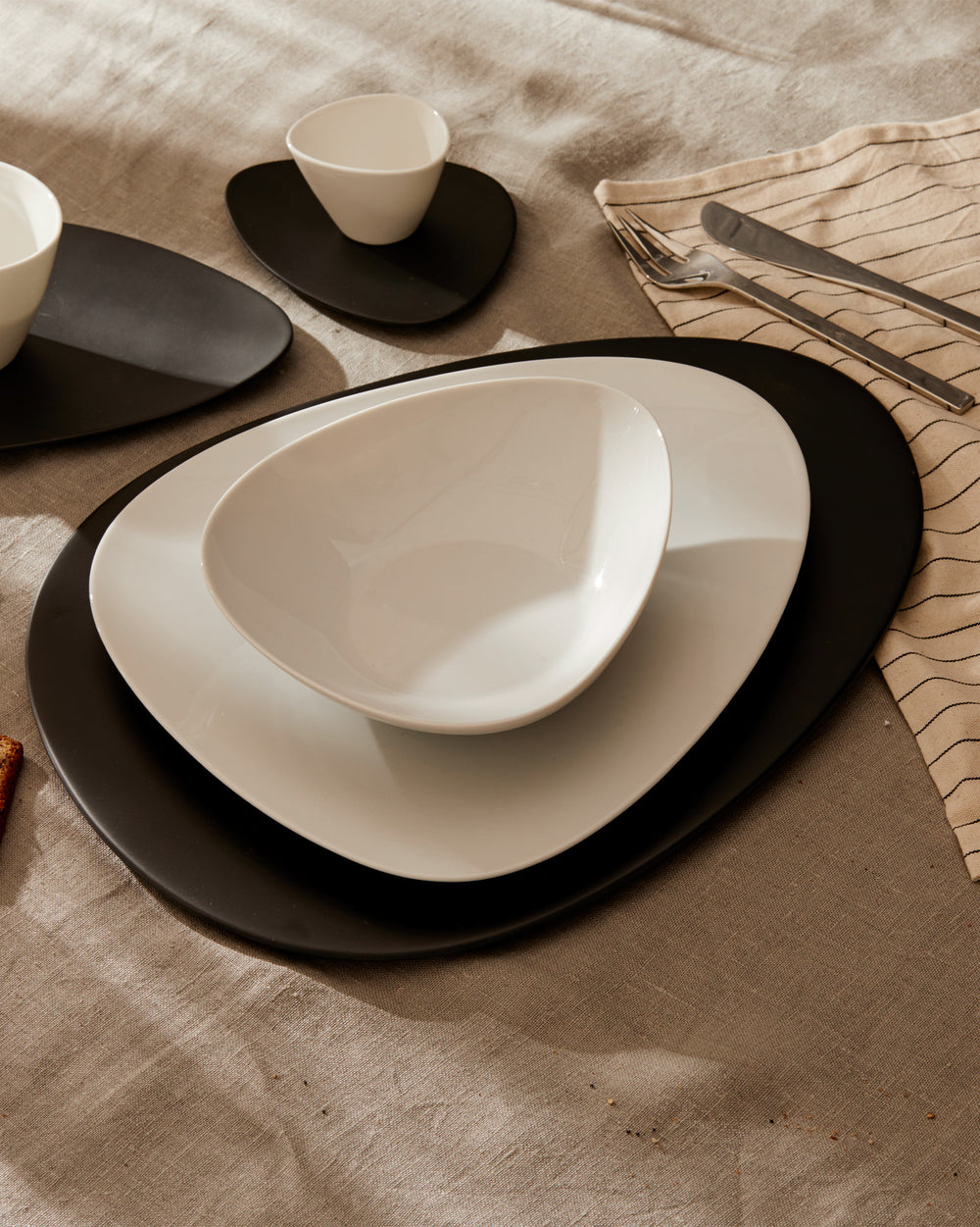 White and black irregular dinnerware set by Alessi, featuring plates and bowls on a textured linen tablecloth.
