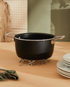 Chrome-plated tripod trivet by Alessi, featuring a collapsible jack-like design, supporting a black pot.