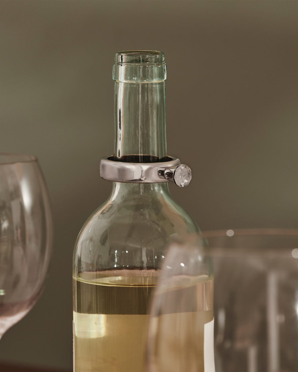 Silver wine bottle collar by Alessi, featuring a clear faceted stone, on a white wine bottle.