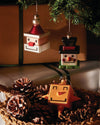 White and red Santa Cube ornament by Alessi, hanging next to a snowman ornament and pinecones.