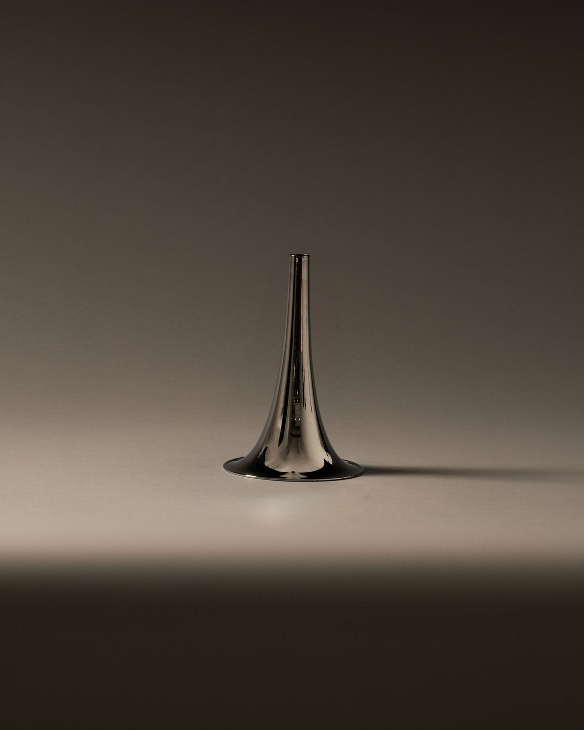 Silver metallic trumpet-shaped vase by Alessi, upright on a soft gradient background.