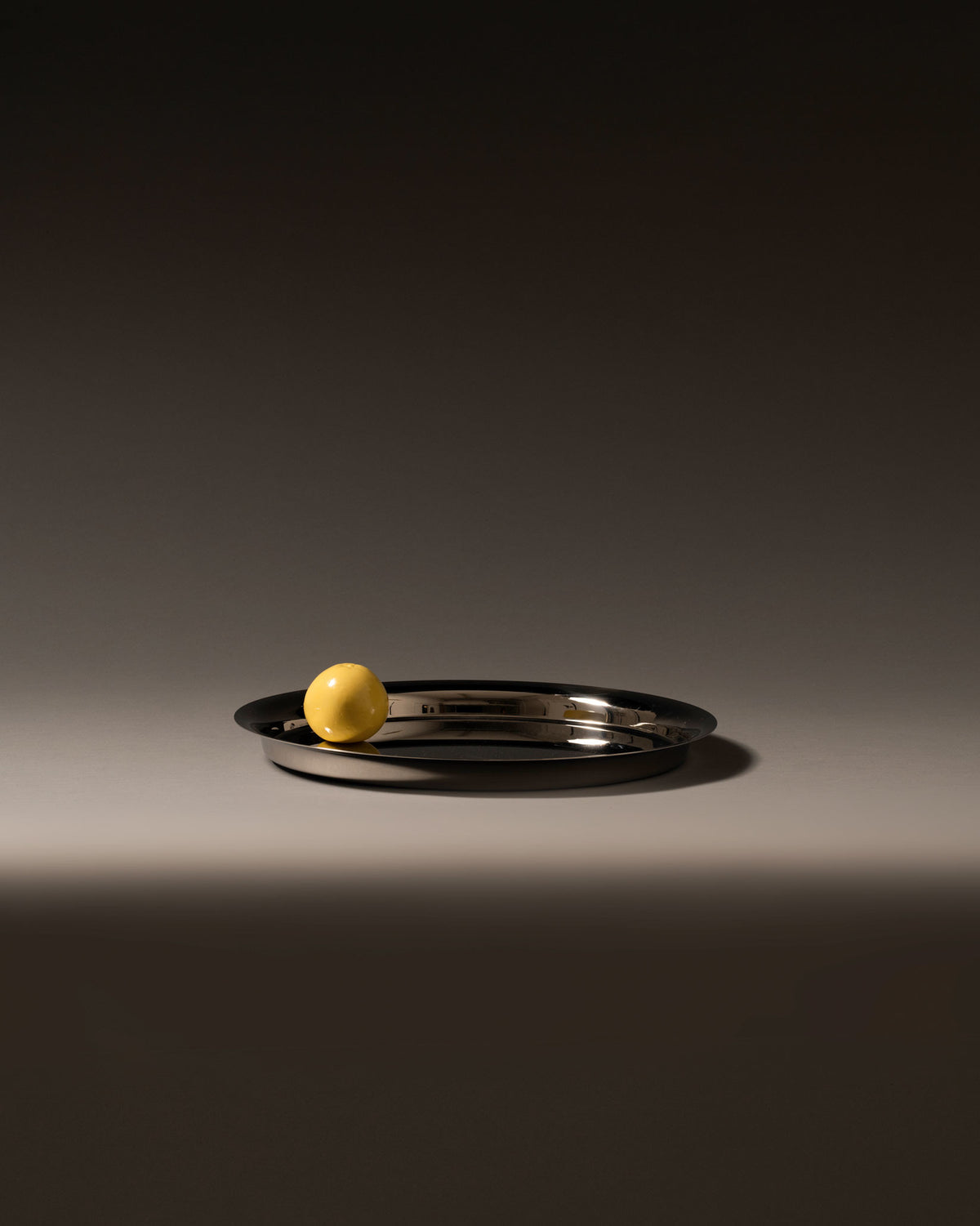Silver oval metal tray by Alessi with a high-shine finish, featuring a single yellow sphere.