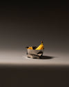 Silver stainless steel fruit bowl by Alessi with a crinkled design, holding two ripe bananas.