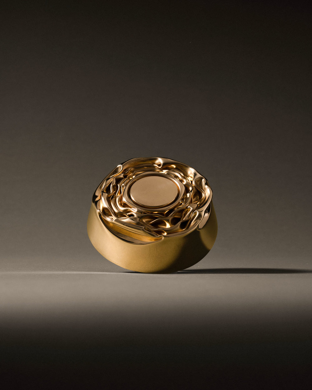 Golden metallic Compressioni container by Alessi, with a wavy, sculptural lid and smooth rounded body.