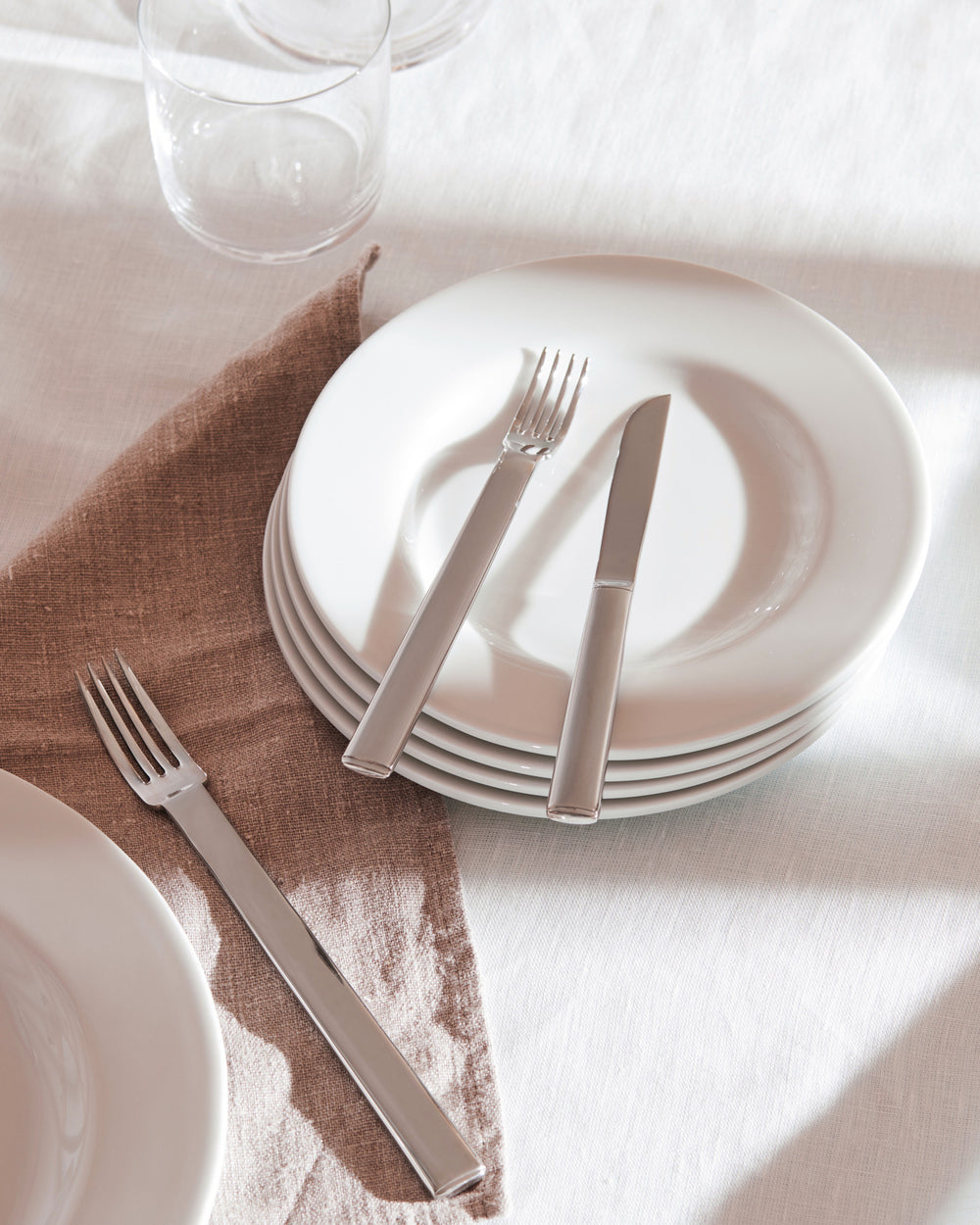Sleek silver cutlery by Alessi, a fork and knife on white plates with a brown linen napkin.