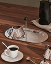 Polished stainless steel coffee and sugar set by Alessi, featuring a conical pitcher with a blue handle and an oval tray.