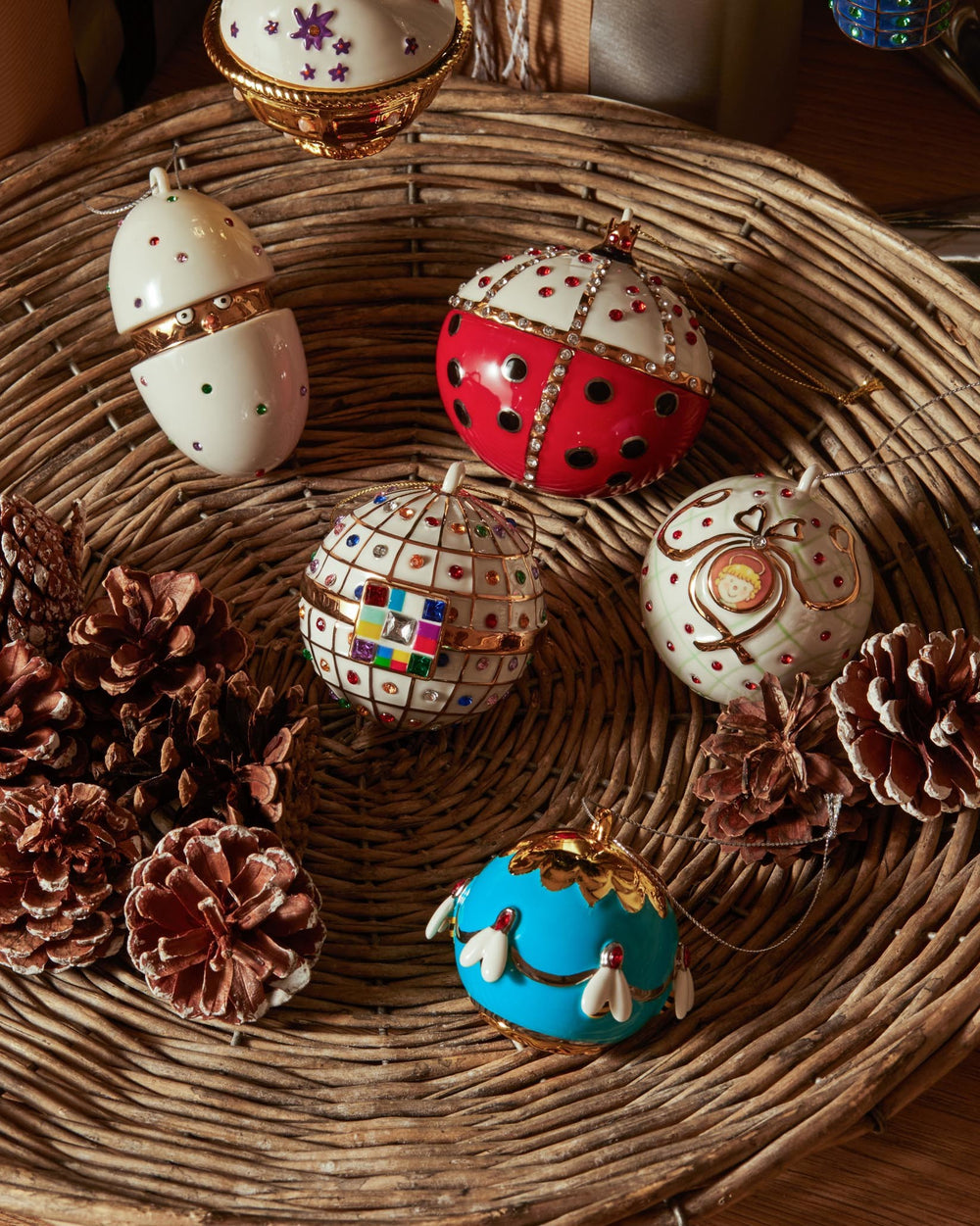Blue spherical ornament with white bees and gold accents by Alessi, resting in a woven basket with pinecones.