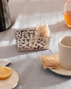 Silver metal tea bag holder by Alessi, featuring a modern cutout cactus design, filled with tea bags on a blue linen tablecloth.