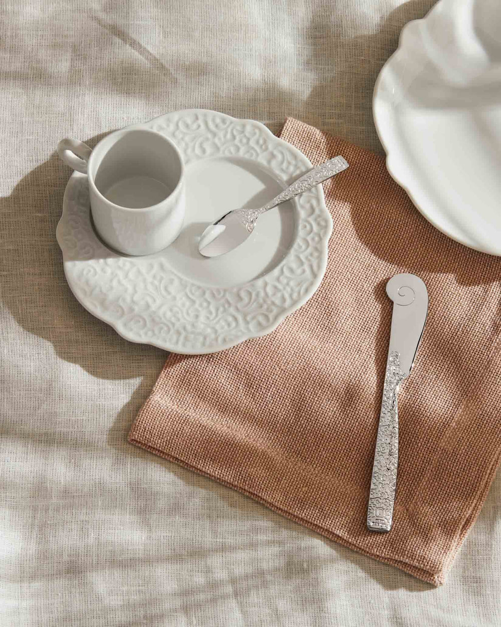 Silver butter knife and spoon by Alessi with ornate embossed handles and a unique curled tip.