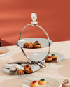 Silver folding tiered serving stand by Alessi, featuring a clown finial and various cookies.