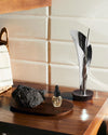 Silver metallic Lily incense holder by Alessi, holding a dark stick, on a polished wooden surface.