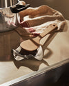 Silver wavy spoon rest by Alessi, holding a wooden spoon on a kitchen counter beside a pot and striped towel.