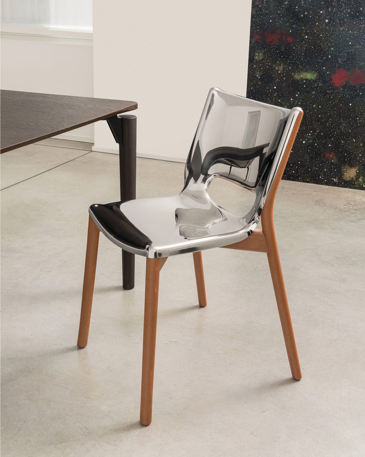 Modern clear chrome-effect chair with natural wood legs by Alessi, positioned at an angle in a contemporary room.