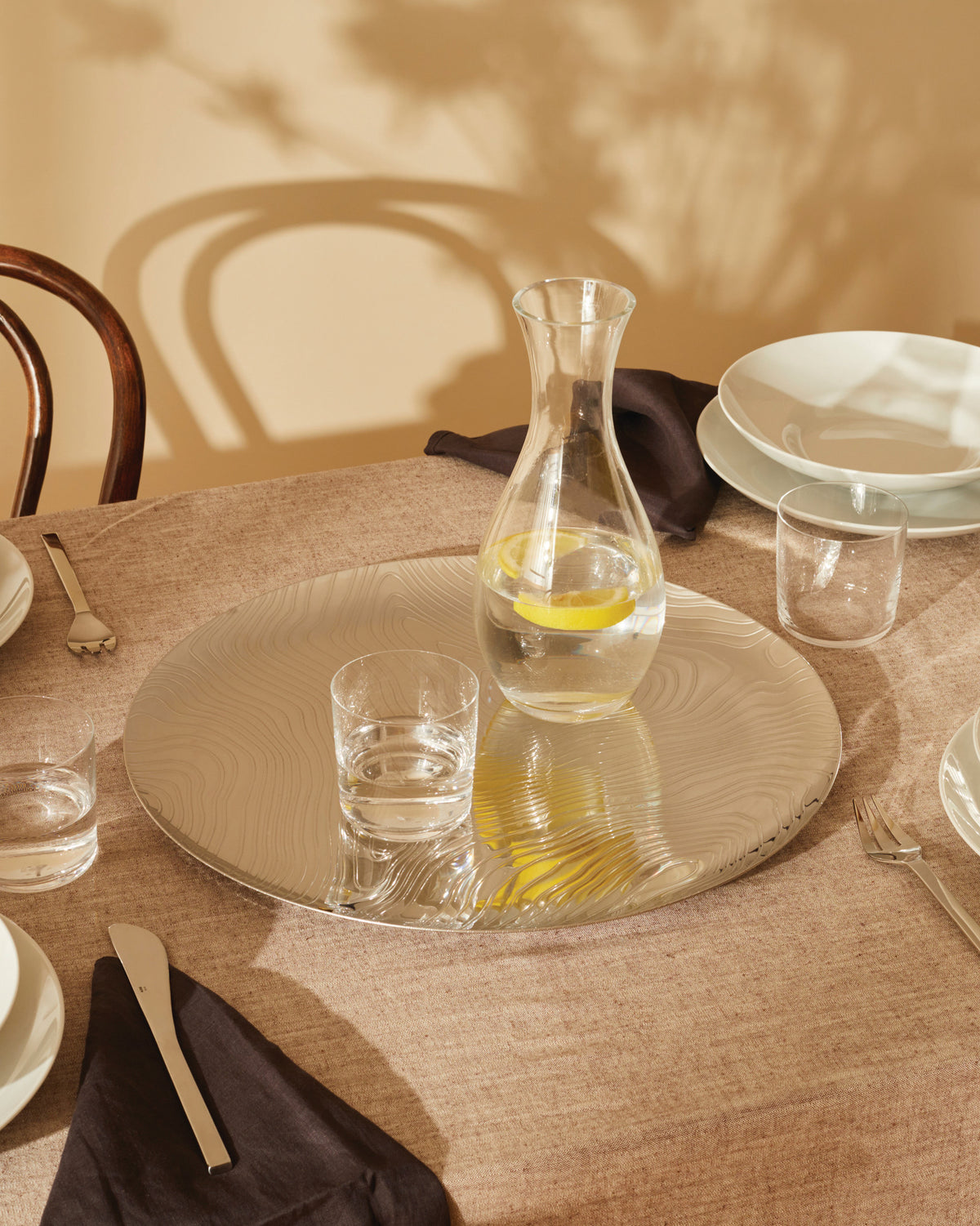 Round silver Veneer platter by Alessi with wavy woodgrain pattern reflecting lemons.