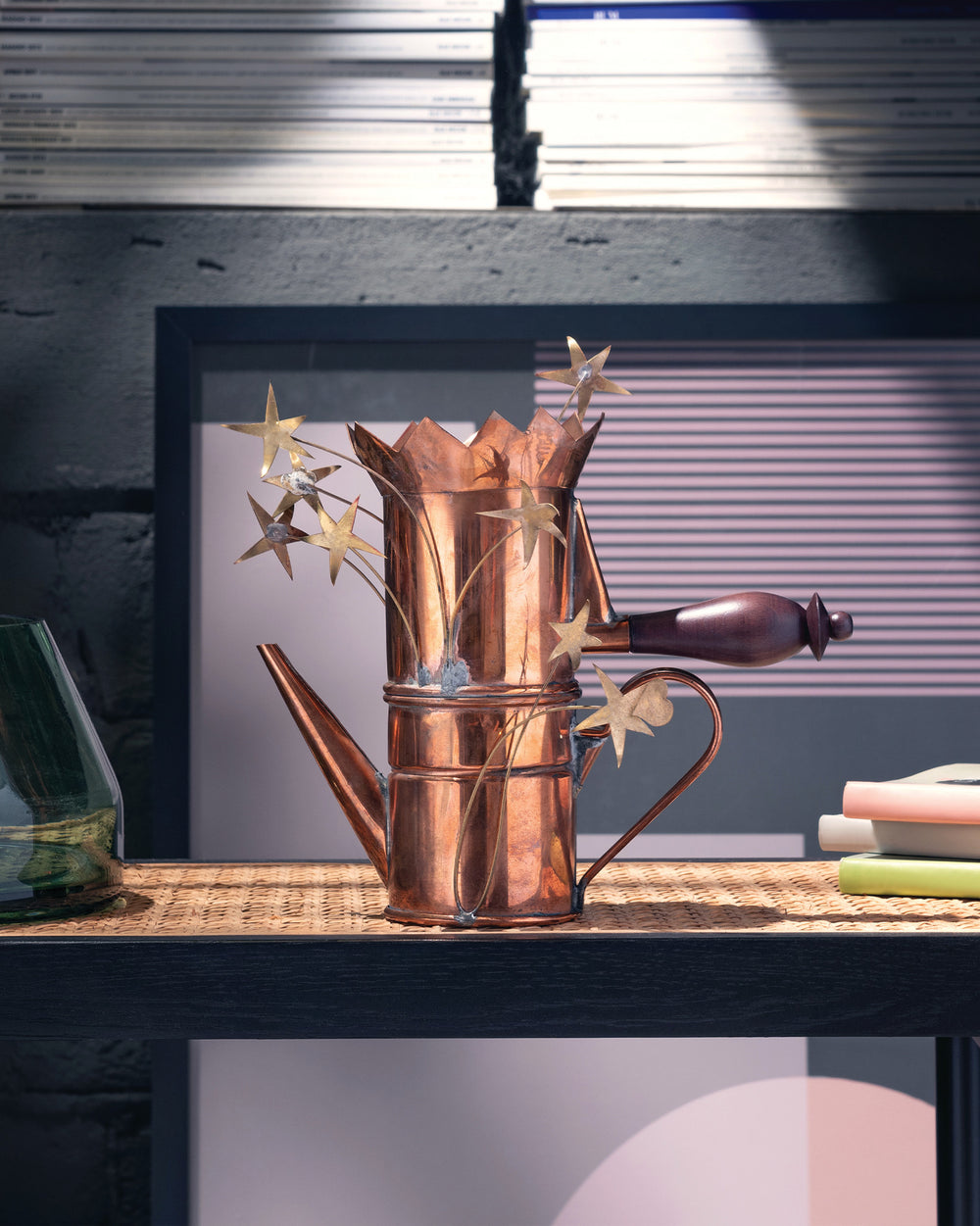 Copper coffee maker with heart and stars by Alessi, displayed on a woven shelf.