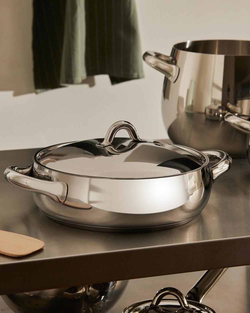 Stainless steel casserole by Alessi with a shiny finish, matching lid, and elegant oval handles.