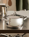 Stainless steel pot with lid by Alessi, with a shiny finish on a metallic kitchen counter.