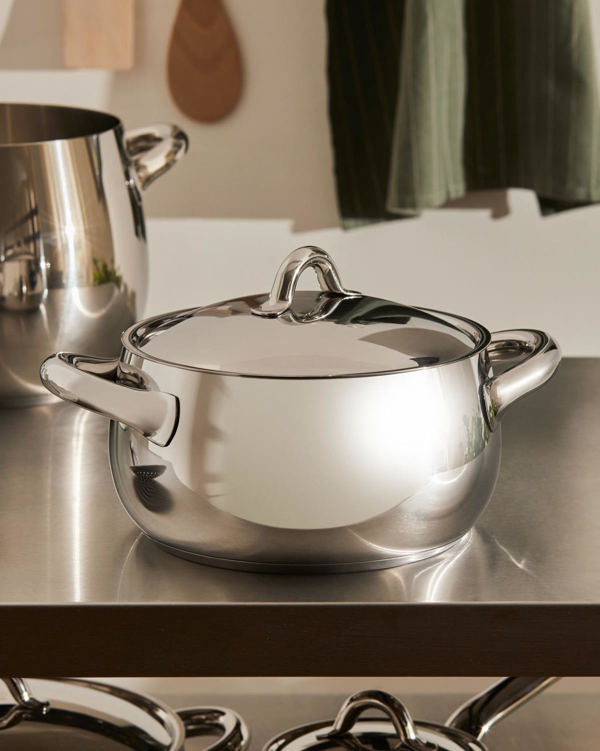 Stainless steel pot with lid by Alessi, with a shiny finish on a metallic kitchen counter.