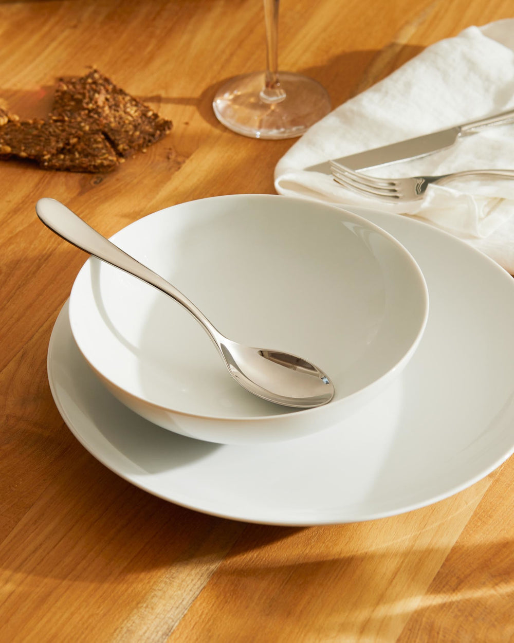 White, smooth bowl by Alessi stacked on a white dinner plate with a spoon, on a wooden table.