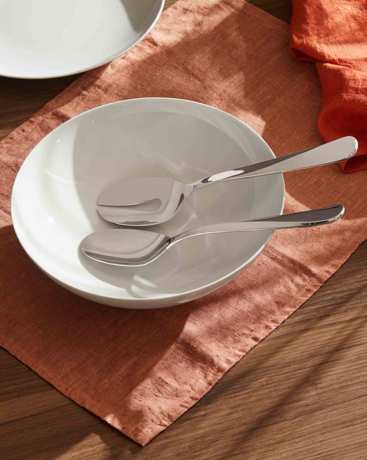 Mami stainless steel serving set by Alessi, polished and resting in a white bowl on an orange linen napkin.
