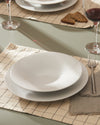 White ceramic plates by Alessi, stacked on a checkered placemat with a fork and wine glass.