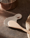 Organic-shaped, glossy silver-toned spoon rest by Alessi, with a wooden spoon on a dark stone surface.