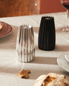 Silver and black pleated grinders by Alessi on a dining table with bread and wine.