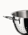 Shiny stainless steel colander by Alessi with a sleek handle and perforated holes, close-up side view.