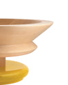Light wood pedestal bowl by Alessi with a smooth, tapered upper section and a bright yellow glossy base, side view.
