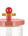 Cropped close-up of a clear glass storage jar by Alessi with a colorful lid featuring a red ball knob and golden disk.