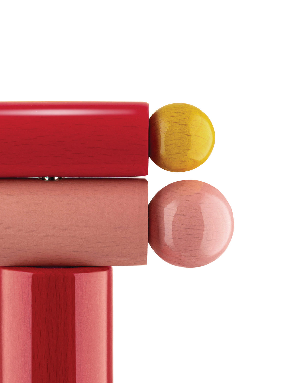 Polished wooden geometric shapes by Alessi, in red, pink, and yellow, showing stacked blocks and spheres.