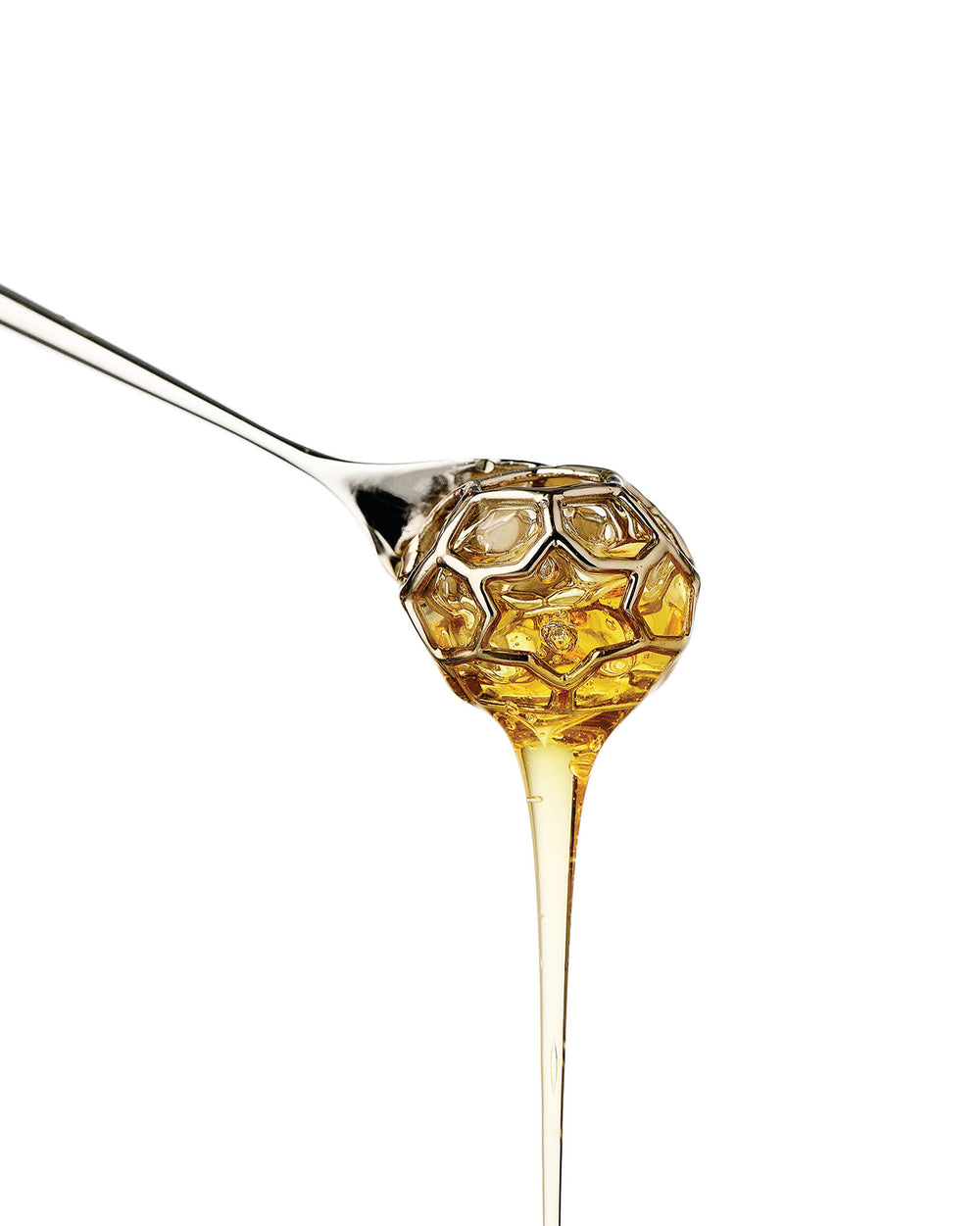 Silver-toned hexagonal honey dipper by Alessi, dripping golden honey against a white background.
