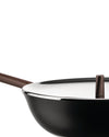 Matte black wok pan by Alessi with a brown handle, shiny silver rim, and a reflective white lid with a brown knob, close-up.