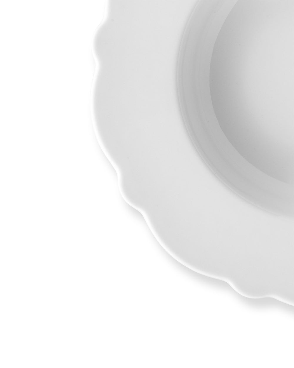 White scalloped plate by Alessi, partially cropped, showcasing its elegant wavy edge.