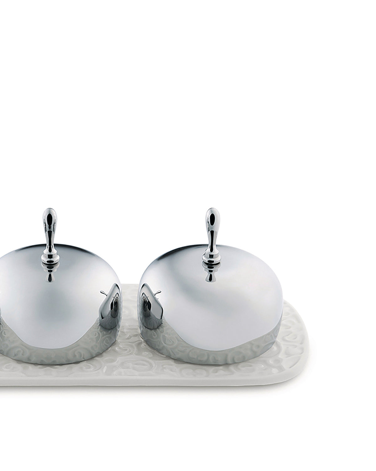 Two chrome butter dishes by Alessi with white embossed ceramic bases on a matching tray.