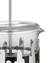 A clear glass French press coffee maker by Alessi, featuring a silver wavy metal frame, filled with coffee.