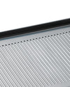Silver-toned metal grate by Alessi featuring narrow parallel slits and a dark top edge, viewed from an angle.