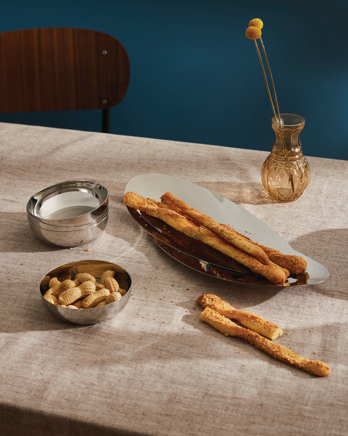 Silver stackable stainless steel bowls by Alessi, with two stacked and one holding peanuts on a beige tablecloth.