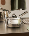 Sleek stainless steel saucepan by Alessi, with a matching lid and long handle, on a metal counter.
