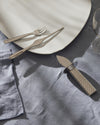 Silver-toned fish cutlery set by Alessi with a scale pattern, displayed on a white plate and blue linen.